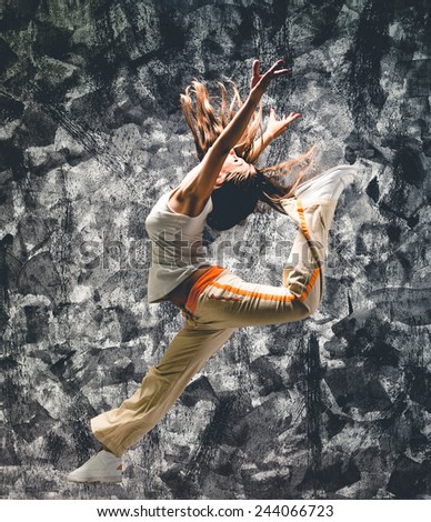 Young woman dancer jumping. On grunge wall background.