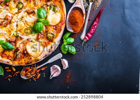 tasty pizza on a black background with spices and vegetables
