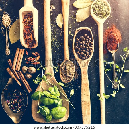 wooden spoons with spices and herbs on textured black background