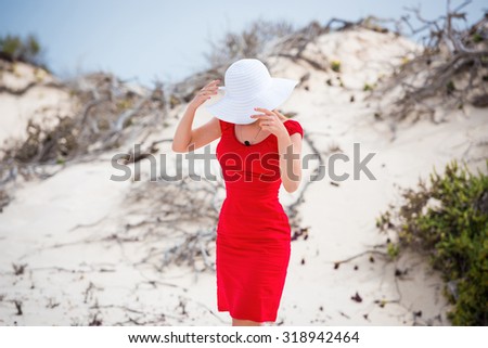 beautiful young woman in evening red dress and white hat on a background of a sand desert