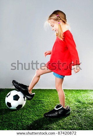 girl with soccer ball in boots on a green lawn