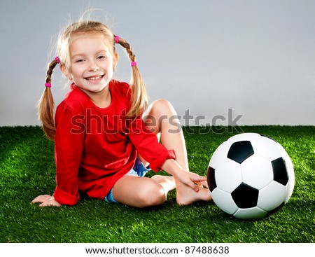little girl with soccer ball in boots on a green lawn
