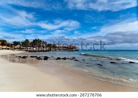 A sandy beach view with stones, blue water and a lighthouse with a restaurant in the background