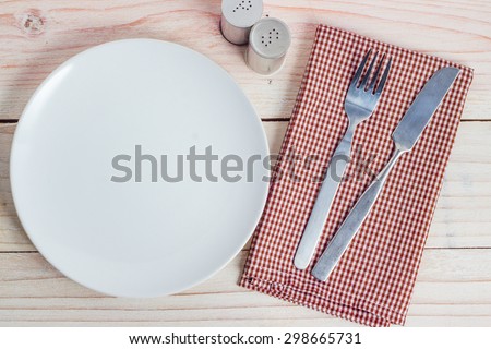 Empty white plate and silverware on white wooden table background
