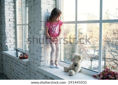 Child in the class for the ballet standing at the window with her hands folded in the shape of heart