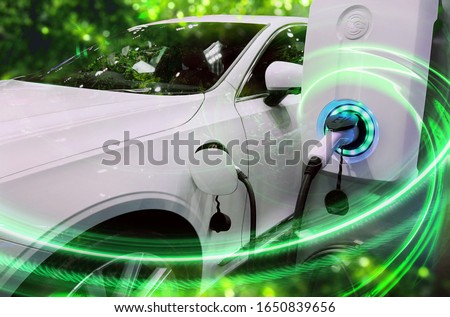 EV Car or Electric vehicle at charging station with the power cable supply plugged in on blurred nature with green enegy power effect. Eco-friendly sustainable energy concept.