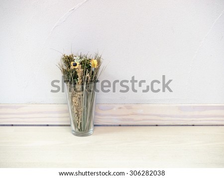 dried flowers and grasses in transparent glass over wooden table with concrete wall background