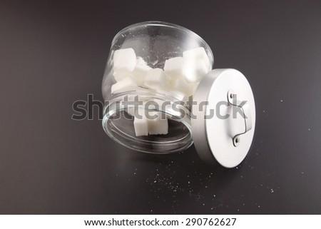 White lump sugar in a glass jar on a gray background, sweet sugar in ware with a glass opened, nobody.