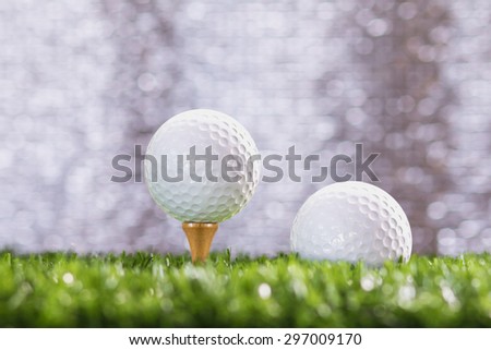 Golf ball on a tee peg and Golf ball on grass, bokeh background silver.