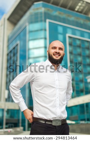Smiling businessman with beard in white shirt standing near office building
