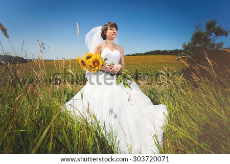Beauty bride in field with bouquet from sunflowers