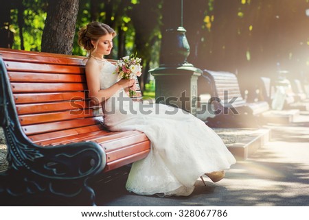 Bride with bouquet sitting on old-fashioned bench in park