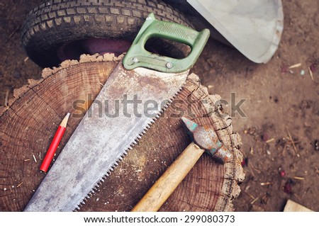 The working tool on a backyard in retro style. The saw, a pencil and a hammer lie on hemp.