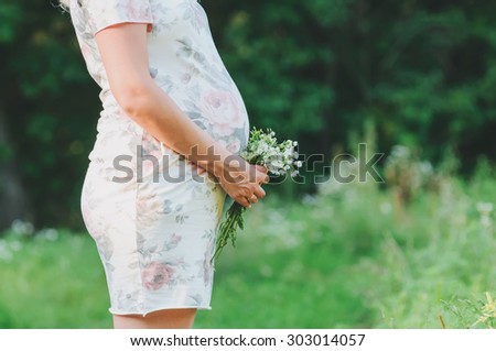 The young pregnant girl embraces the stomach. In hands a bouquet from wild flowers.