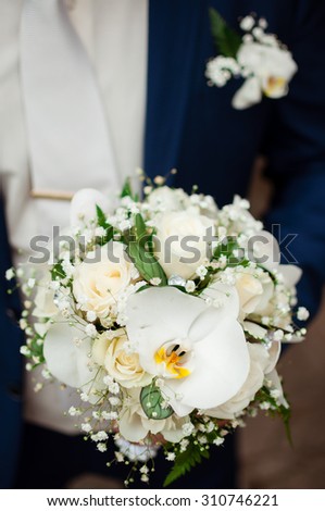 The groom holds a bridal bouquet in hand. A bouquet of flowers from lilies and white roses.