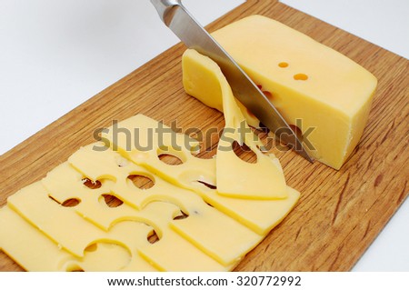 The sliced cheese with big holes lies on a table with a knife and a big piece of cheese.