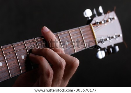 Male hand holding a barre on the acoustic guitar, close-up on a black background