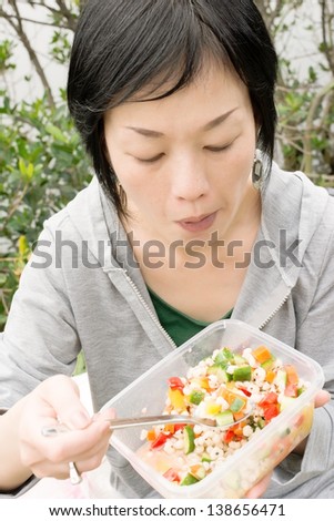 Mature Asian woman eat salad in outdoor park in daytime.