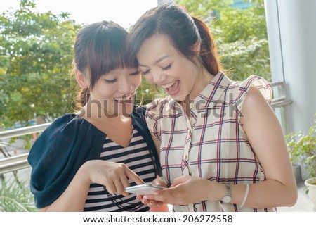 Group of smiling Asian women looking at something on a cellphone.