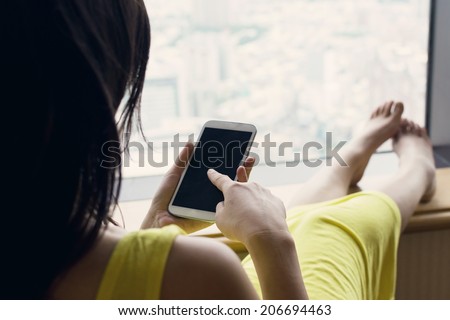 Asian woman sit on chair facing the window and using cellphone at vacation.
