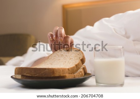 Woman's hand reaching from under duvet for breakfast in hotel.