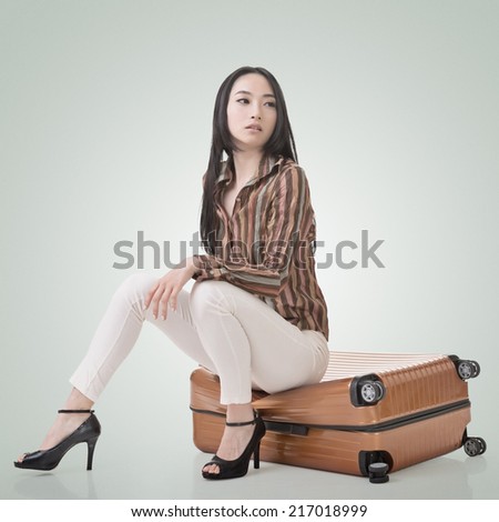 Asian woman thinking and sitting on a luggage.