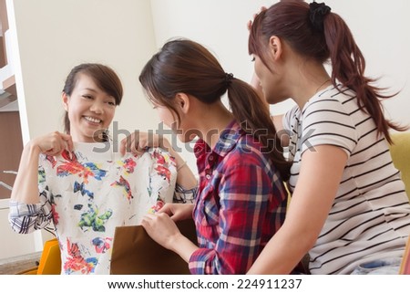 Beautiful young woman showing her brand new clothes to her friend in the room.