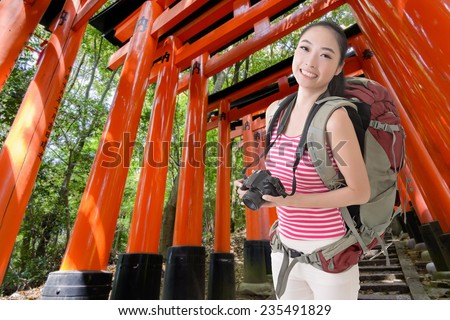 Happy smiling Asian young female backpacker with camera in Fushimi Inari Taisha, Japan.