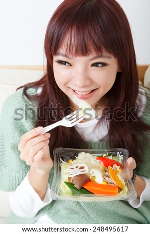 Young girl eating salad with smiling expression at home.