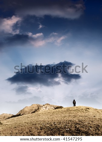Man in lonely walk to mountain on the hill in outdoor under the dramatic sky and clouds.