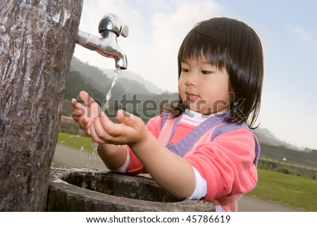 Asian baby with black hair and yellow skin wash hand in outdoor of park.