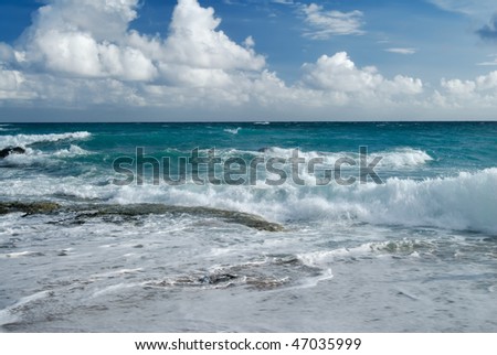 Beach with dramatic sea wave under blue sunny sky.