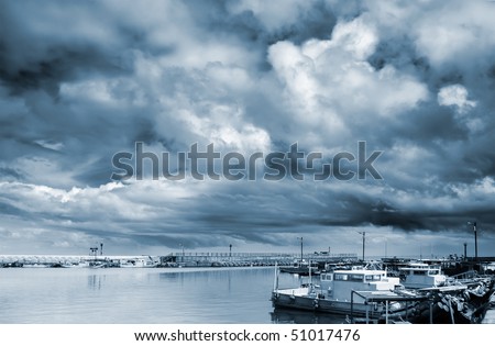 Storm clouds with boats on sea port.