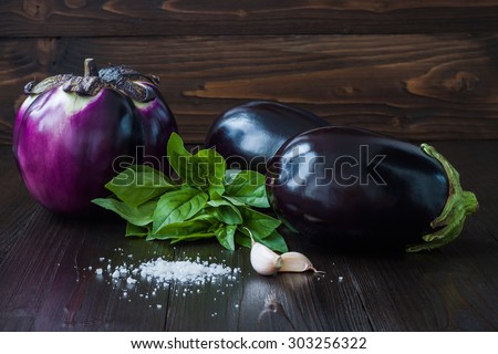 Eggplant (aubergine) with basil and garlic on dark wooden table. Fresh raw farm vegetables - harvest from the garden in rustic kitchen. Rural still life