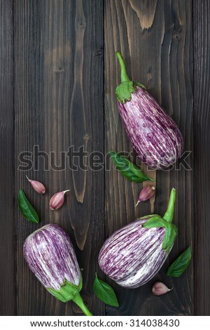 Purple eggplant, garlic and basil leaves from above on the old wooden board with free text space. Fresh harvest from the garden. Top view