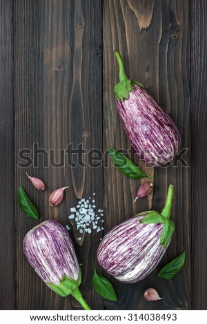 Purple eggplant, garlic and basil leaves from above on the old wooden board with free text space. Fresh harvest from the garden. Top view