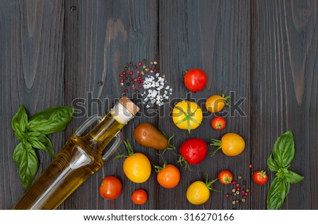 Cherry tomatoes of various color, basil leaves, spices and olive oil from above over dark wooden table. Italian caprese salad recipe ingredients. Top view, free text copy space