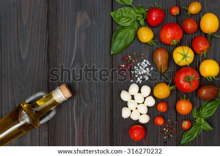 Cherry tomatoes of various color, mozzarella, basil leaves, spices and olive oil from above over dark wooden table. Italian caprese salad recipe ingredients. Top view, free text copy space