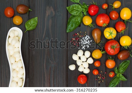 Cherry tomatoes of various color, mozzarella, basil leaves, spices from above over dark wooden table. Italian caprese salad recipe ingredients. Top view, free text copy space