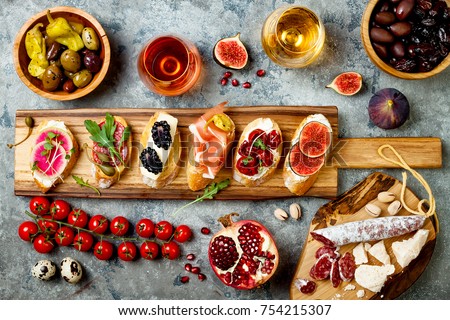 Appetizers table with italian antipasti snacks and wine in glasses. Brushetta or authentic traditional spanish tapas set, cheese variety board over grey concrete background. Top view, flat lay Foto stock © 