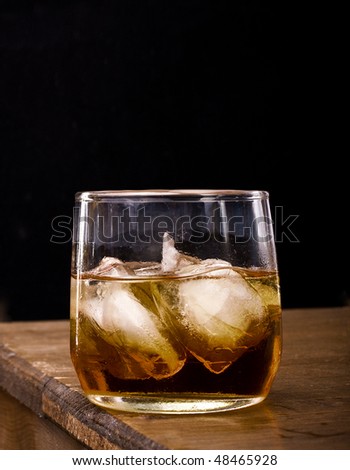 Glass of whiskey, scotch or bourbon on the rocks placed on top of a wooden bar with black background and dark ambiance for vintage look