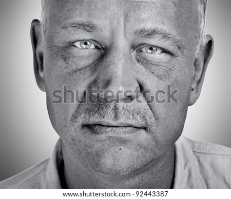 Closeup black and white artistic character portrait of a rough looking handsome man in his forties with piercing light blue eyes looking at the camera with questioning and suspicious facial expression