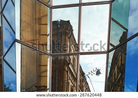 Office building with a mirror coating . Details of the urban landscape are reflected in the windows of the building. Mixing modern and old buildings. Windows - quirky geometric designs .