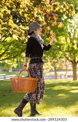 An Asian young lady carrying a picnic basket, golden tree leaves lit by the low sunlight  in sunset