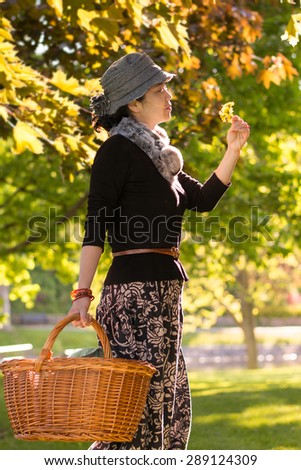 An Asian young lady carrying a picnic basket, golden tree leaves lit by the low sunlight  in sunset