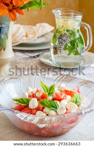 Capri salad on a summer time dinner table. Bouquet in vintage English vase. Bird shaped napkin rings. In bright natural light. Herbal tea in vintage jar. Red, green, white.