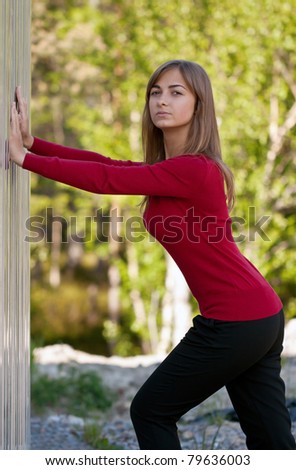 Beautiful girl in purple dress outside steel wall against the background of the forest