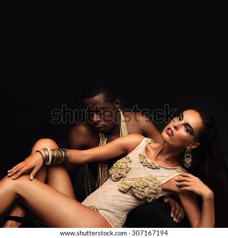 Fashion studio photo of a sensual couple;  woman in a gold swimsuit handmade with her man  on black background