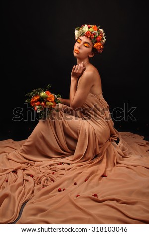 Portrait of beautiful woman with stylish makeup and colorful flowers around her head and smelling a bouquet with pleasure on a dark background in the studio. The concept of friendly autumn.