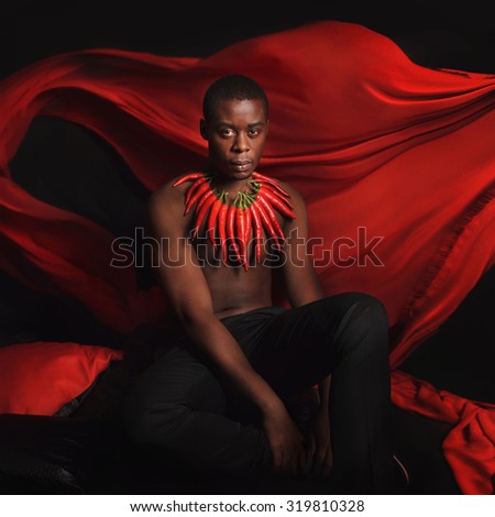 The man with red hot and spicy pepper. Model with creative food vegetables make up on a black background with red flying textile.